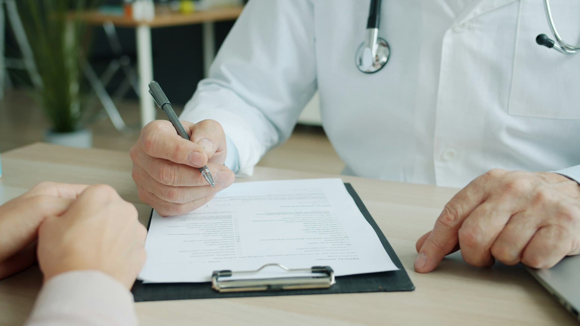 A doctor writing notes while a patient sits opposite